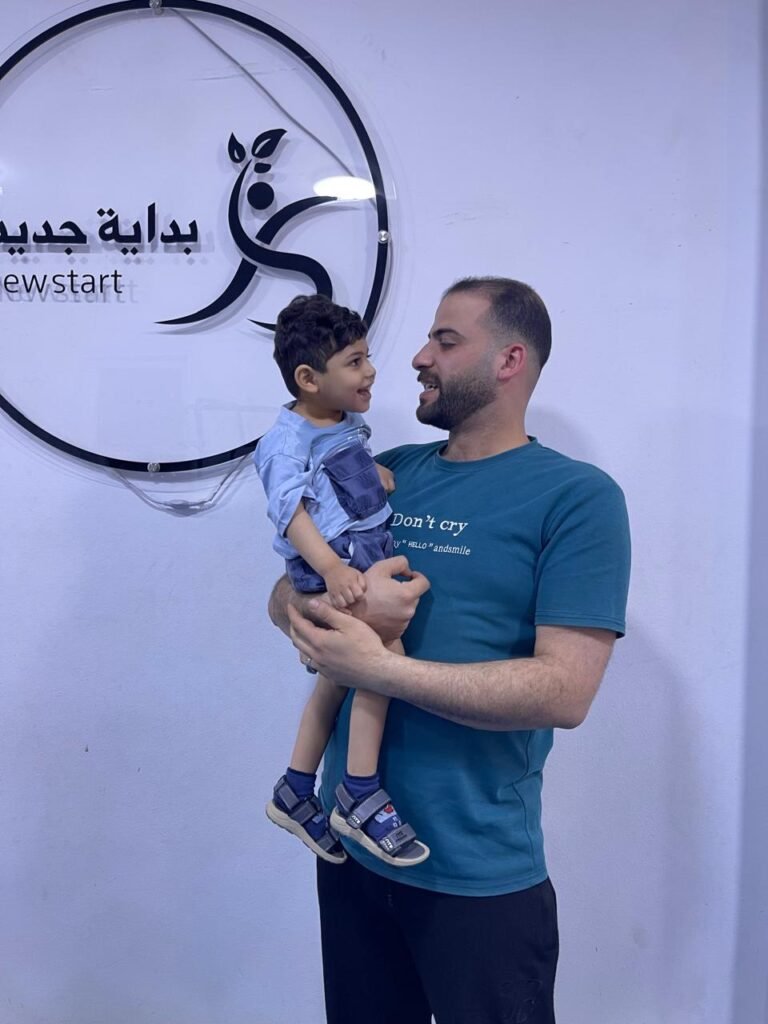 أخصائي يحمل طفلًا أمام شعار مركز بداية جديدة