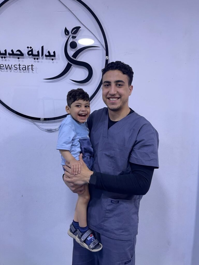 أخصائي يرتدي الزي الطبي مع طفل مبتسم أمام شعار المركز